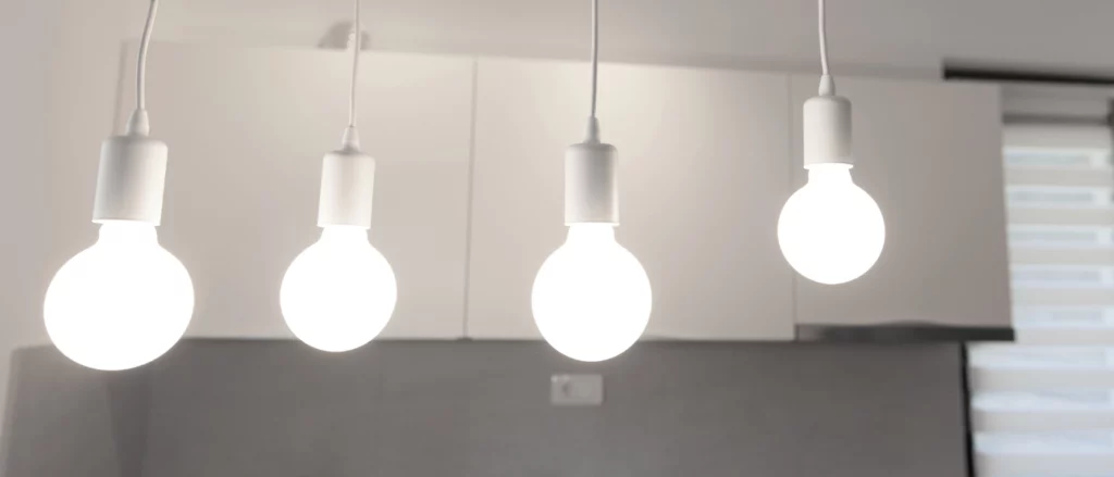 Four modern hanging light bulbs in white fixtures, glowing brightly against a minimal kitchen backdrop.